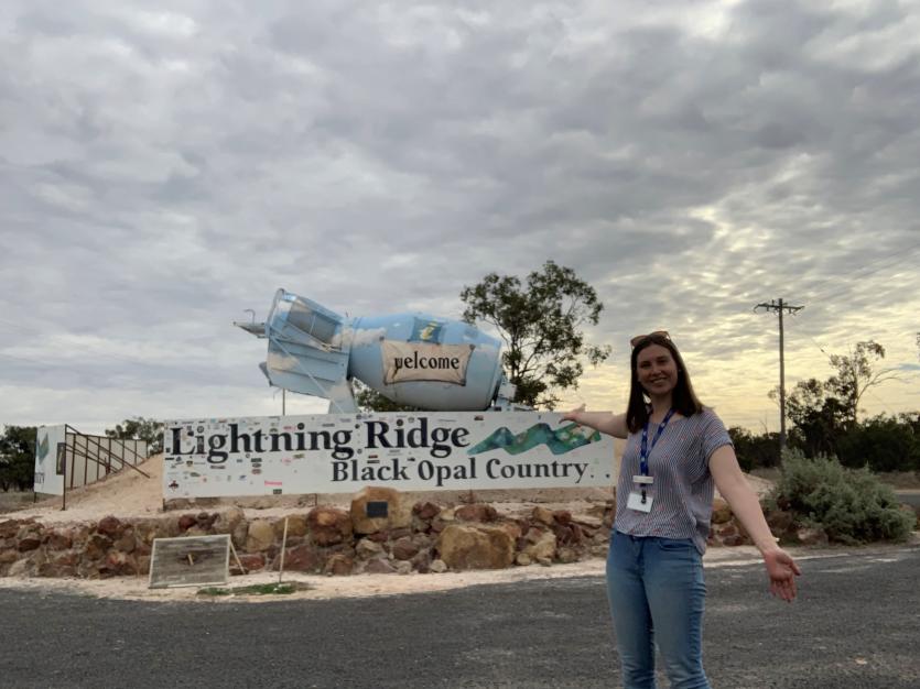 A young woman standing infront of the 'Lightening Ridge' sign
