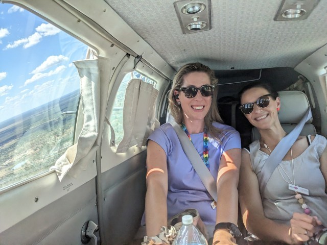 Two female clinicians are sitting in an airplane smiling.