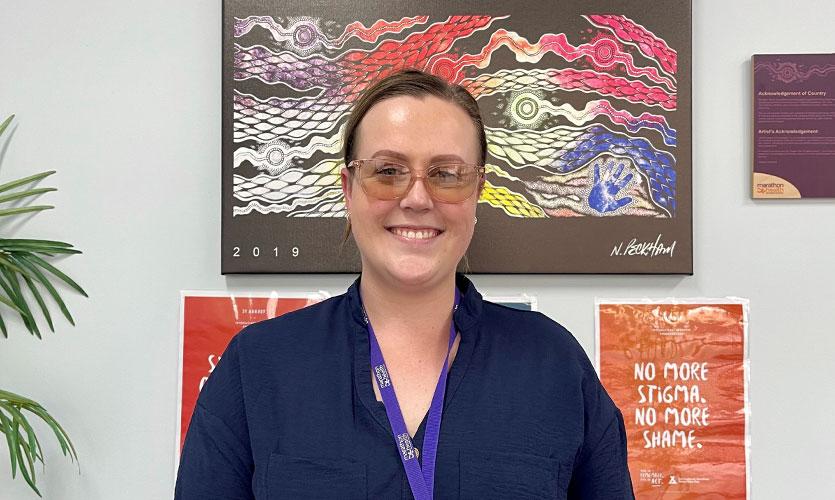 A women is smiling in front of artwork.