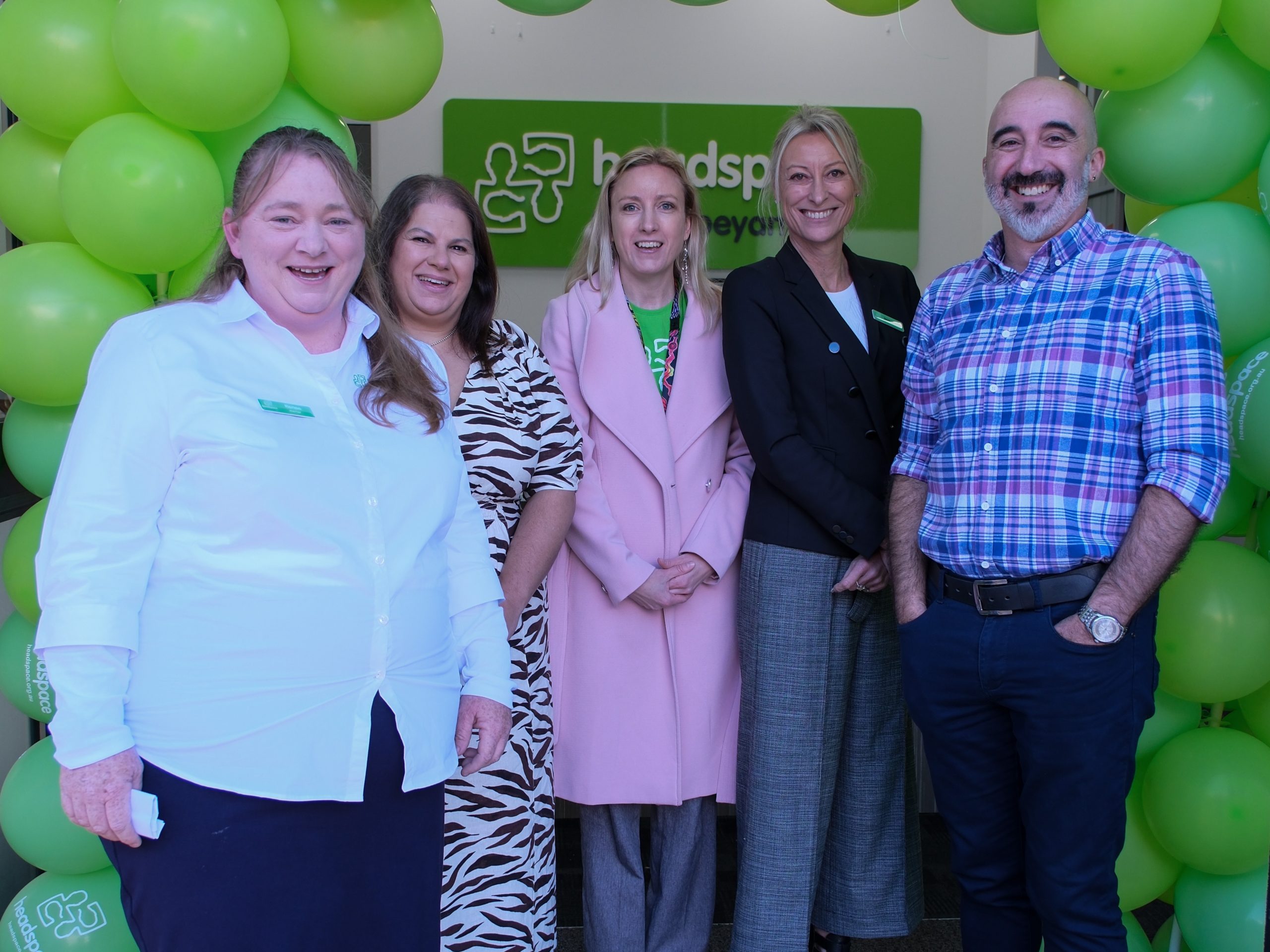 5 headspace staff standing under an arch of green balloons