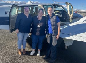 Ella (right) poses in front of the light plane alongside a Marathon Health Speech Pathologist and Occupational Therapist.