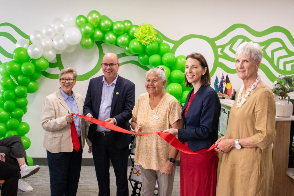 A group of people stand holding a red ribbo, ready to officially open the office
