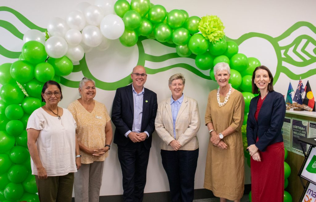 a group of people stand under the green and white balloon arch